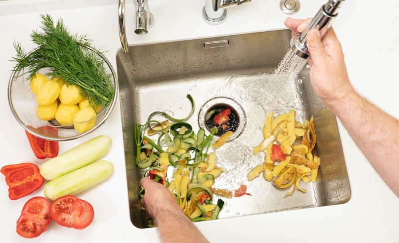 A man recycles food waste using a modern kitchen disposer.