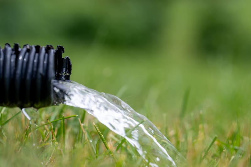 Residential sump pump drain line discharging water into grass yard after a rainstorm . High quality photo
