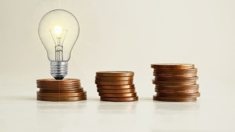 Increasing of electricity cost for residential and business users, expensive energy bill and rise in electricity prices concept. Lots of coins and a light bulb
