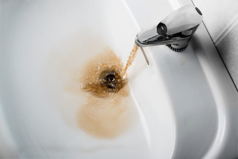 Dirty brown water running into a white sink. Looks very unhealthy,