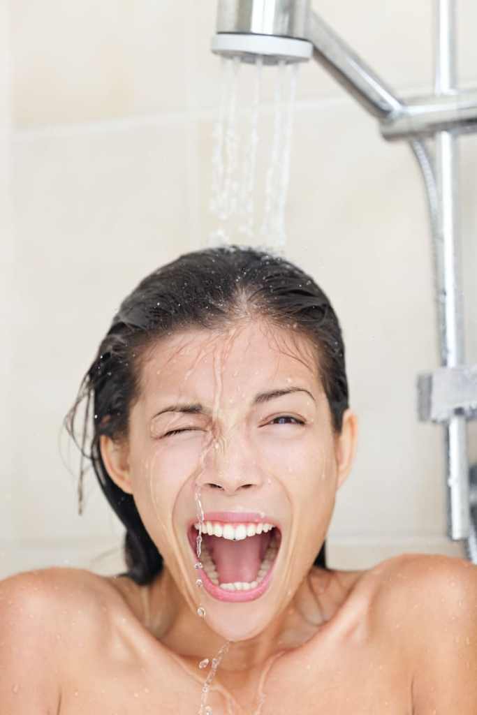 Cold shower. Woman taking ice cold shower screaming funny at camera. Fun image of beautiful young multiracial female model showering in bathroom at home.