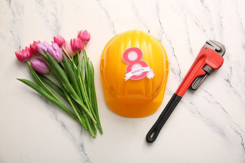 Tulip flowers with plumber's pipe wrench, helmet and paper figure 8 on grunge white background. International Women's Day celebration