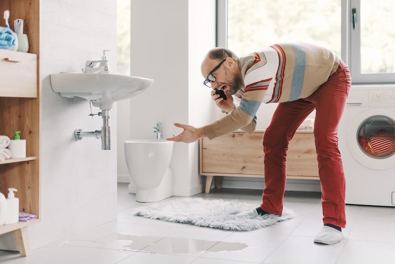 Desperate man calling a plumber with his smartphone, his bathroom sink is leaking