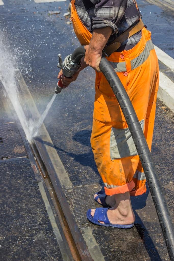 Road worker wearing slippers and using water jet to remove detritus from tram tracks