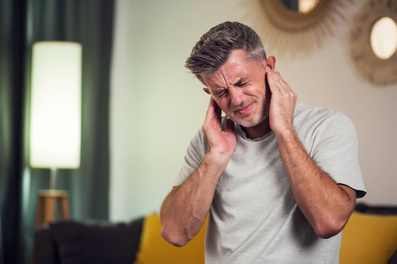 Portrait of man covering his ears, stressed or unhappy because of loud music or too much noise. Indoors shot bc of a loud sump pump