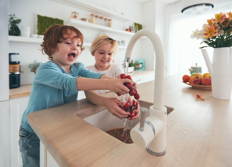 happy kids washing cherries under tap water at the kitchen wasting water hose bib