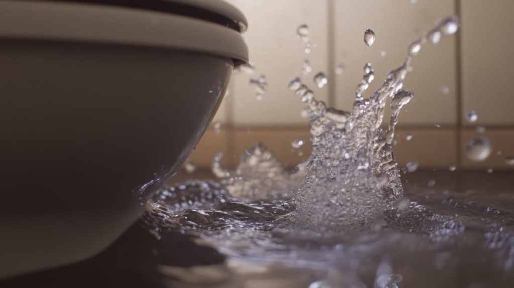 Water splashing from an overflowing toilet in a flooded bathroom, as it spreads across the floor, underscores the need for prompt home insurance coverage