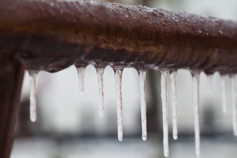 Icicles hanging from a brown pipe. Frozen water and metal surface, winter time concept. selective focus shallow depth field