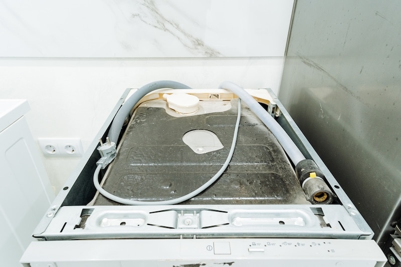 In the kitchen, a dishwasher is currently undergoing repairs, and it has a hose connected to it for the maintenance process or troubleshooting purposes, ensuring it functions properly once fixed