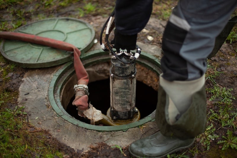 Sewer repair. The worker lowers the equipment into the sewer hatch. Installation of the hydrant in the underground water supply system.